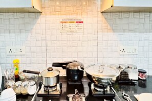 Eine Küche mit Gasherd, Töpfen, Wasserkocher und verschiedenen Küchenutensilien. Eine Anleitung für den Gasherd ist an der Wand sichtbar.
