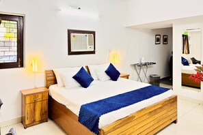 A hotel room with a wooden bed, two bedside tables, a wall-mounted air conditioner, a mirror, and a small ironing station. - Nivera Stays 4BHK Ground Floor Home near Fortis, IGI Airport, South Delhi (New Delhi)
