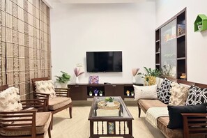 Ein Wohnzimmer mit einer Couch, Sesseln, einem Couchtisch, einem Fernseher und einem Bücherregal.
