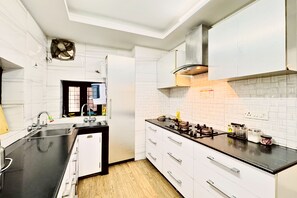 A modern kitchen with white cabinetry, a black countertop, and a gas stove. - Nivera Stays 4BHK Ground Floor Home near Fortis, IGI Airport, South Delhi (New Delhi)