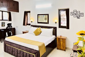 Ein Hotelzimmer mit Bett, Nachttischen, Schreibtisch, Stuhl, Wandklimaanlage und gerahmten Bildern.