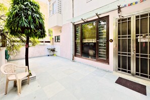 A courtyard with a bench, a small tree, a tiled floor, and a building with large windows and a door. - Nivera Stays 4BHK Ground Floor Home near Fortis, IGI Airport, South Delhi (New Delhi)