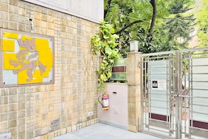 A gated entrance with a fire extinguisher mounted on the wall, a metal gate, and a yellow and white sign. - Nivera Stays 4BHK Ground Floor Home near Fortis, IGI Airport, South Delhi (New Delhi)
