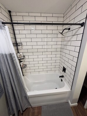 Ein Badezimmer mit einer weißen Badewanne, einer Duschkabine und einer gefliesten Wand.