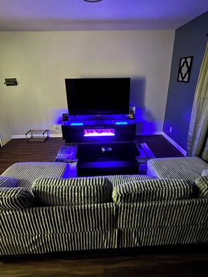 Ein Wohnzimmer mit Flachbildfernseher, Kamin und gestreiften Sofas.