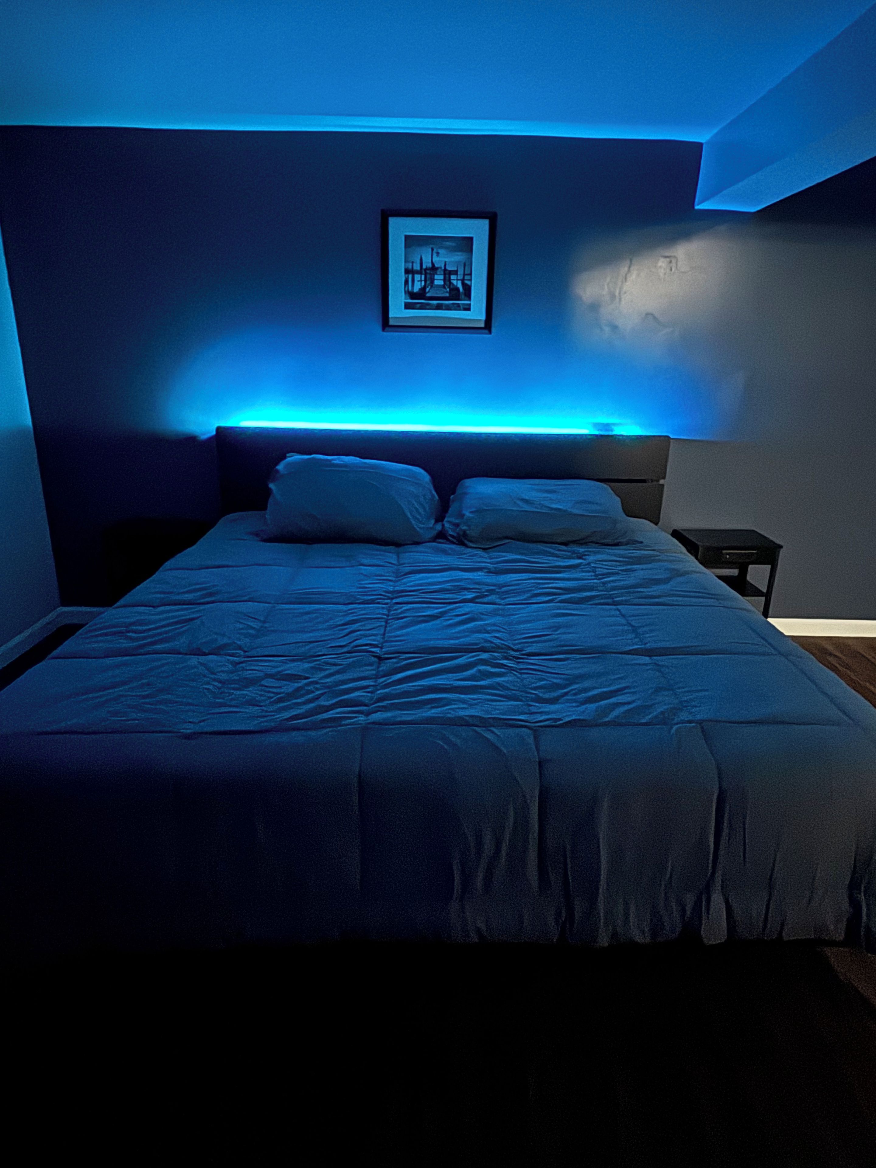 A bed with a headboard, a bedside table, and a framed picture on the wall.