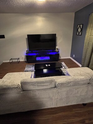 Ein Wohnzimmer mit Flachbildfernseher auf einem Schrank, einem weißen Sofa und Holzboden.