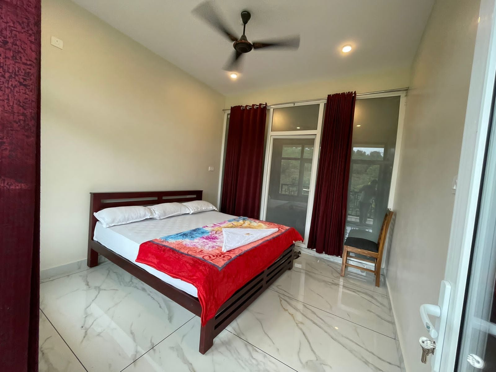 A bedroom with a bed, a ceiling fan, a window with curtains, and a view outside.