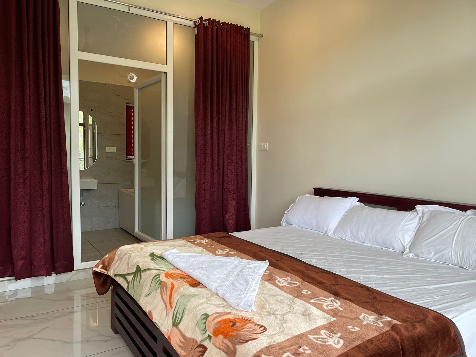 Una habitación de hotel con cama, baño con puerta de vidrio y cortinas rojas.