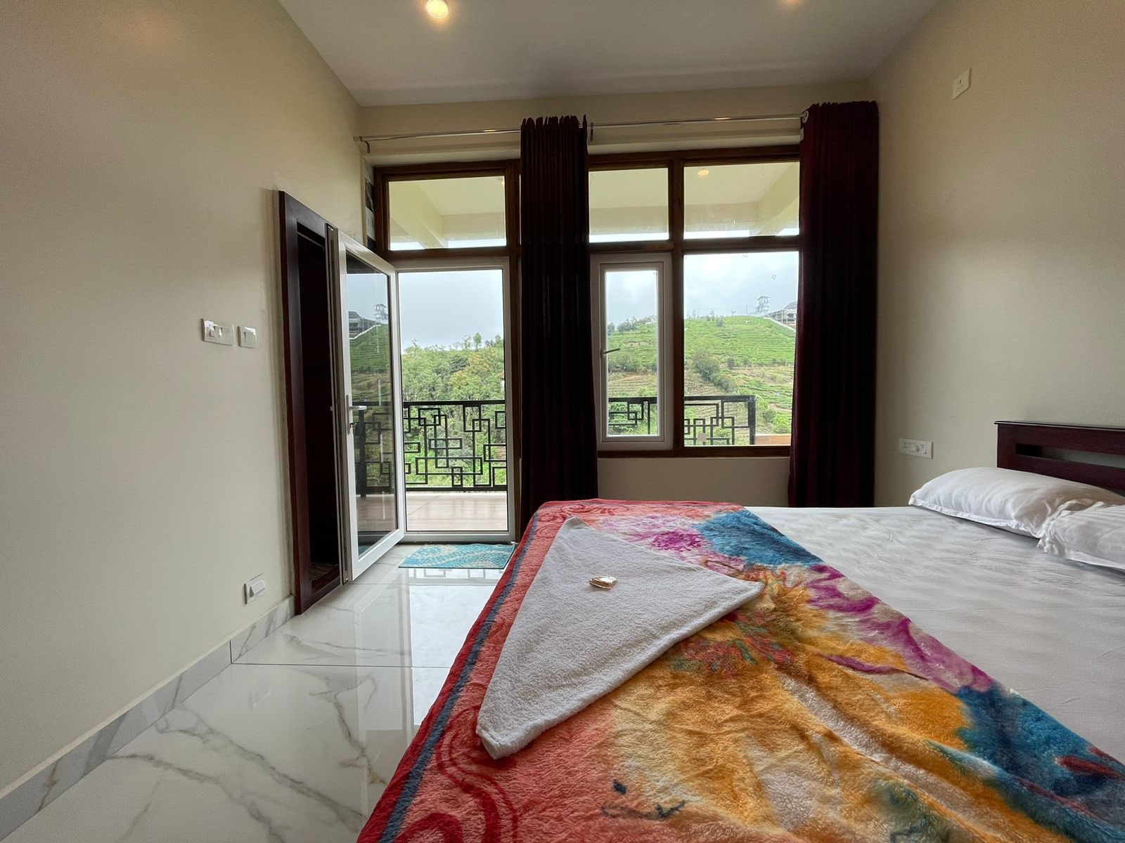 Habitación de hotel con cama, ventana con cortinas, balcón y vista a la vegetación.
