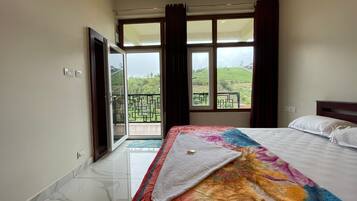 Habitación de hotel con cama, ventana con cortinas, balcón y vista a la vegetación.