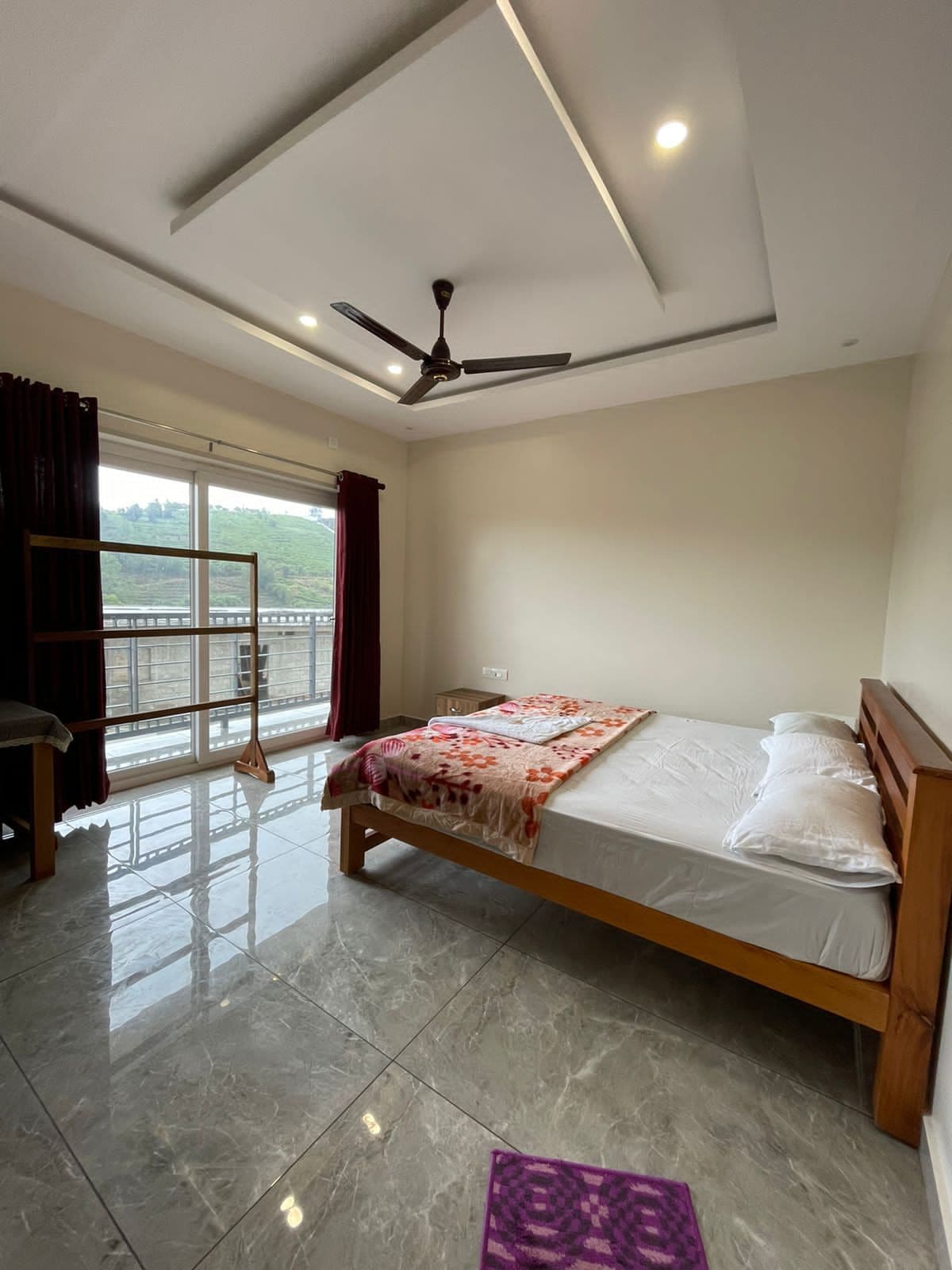 Une chambre à coucher avec un lit, un ventilateur de plafond, une fenêtre avec des rideaux et une vue sur la verdure à l’extérieur.