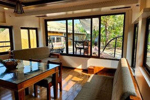 Una habitación con una mesa de comedor de vidrio, sillas de madera, un banco acolchado y ventanas grandes con vistas al exterior.