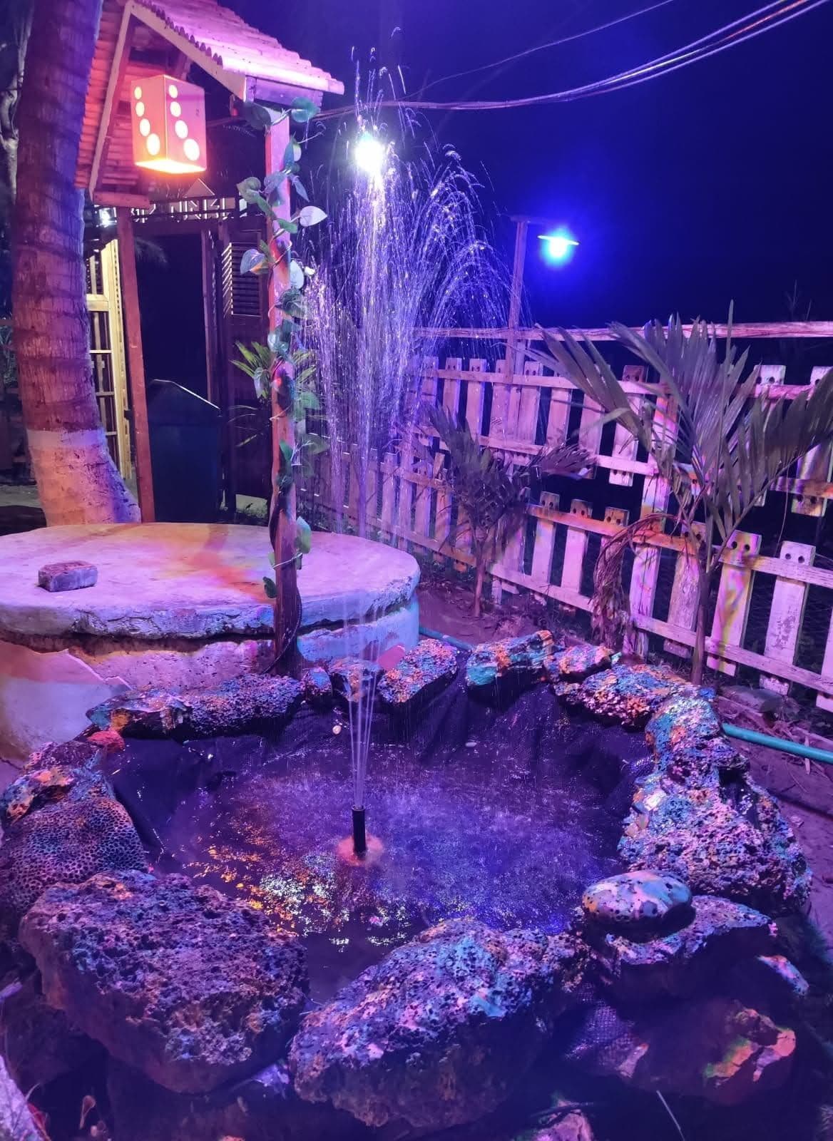 Un élément décoratif aquatique comprenant une fontaine, entouré de rochers et de plantes, et situé sous une structure en bois portant une enseigne.