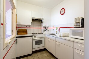 A kitchen with white cabinets, a gas stove, an oven, a microwave, and a red-striped backsplash. - Apartment in Blankenberge by the Beach (Blankenberge)