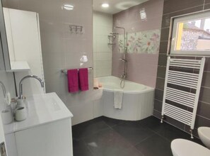 Ein Badezimmer mit einem weißen Waschbecken, einer Badewanne und einer Toilette. Ein Handtuchhalter mit zwei Handtüchern sowie eine Dusche mit Glaswand.