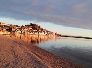Eine Küstenstadt mit Gebäuden an der Uferlinie, einem Sandstrand und ruhigem Wasser, das die Architektur widerspiegelt.