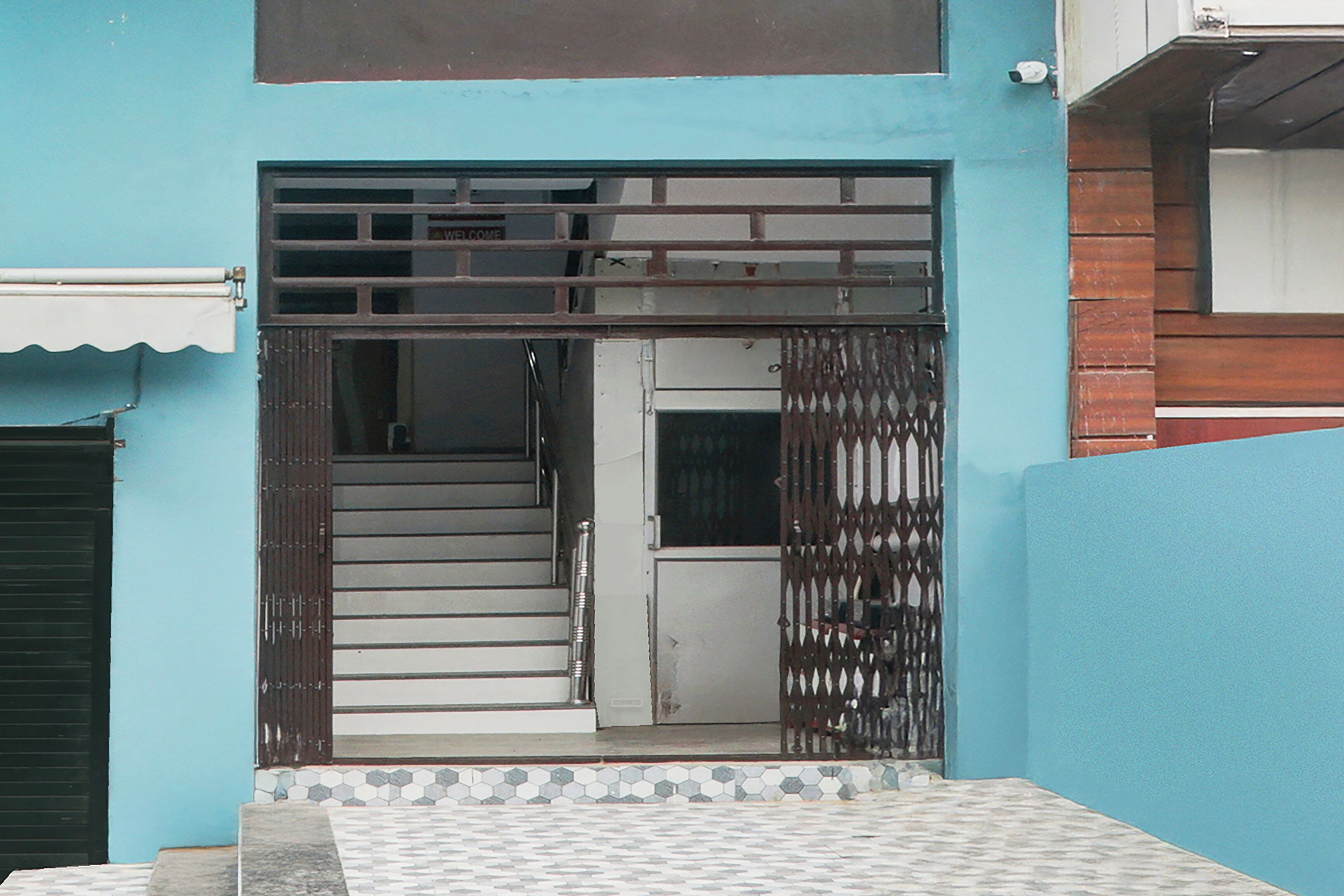 A residential entrance with a metal gate, a staircase leading to a door, and a tiled floor.