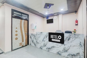 Un espace d’accueil d’hôtel avec un comptoir en marbre, un bureau de réception, un téléviseur fixé au mur et un extincteur accroché au mur.