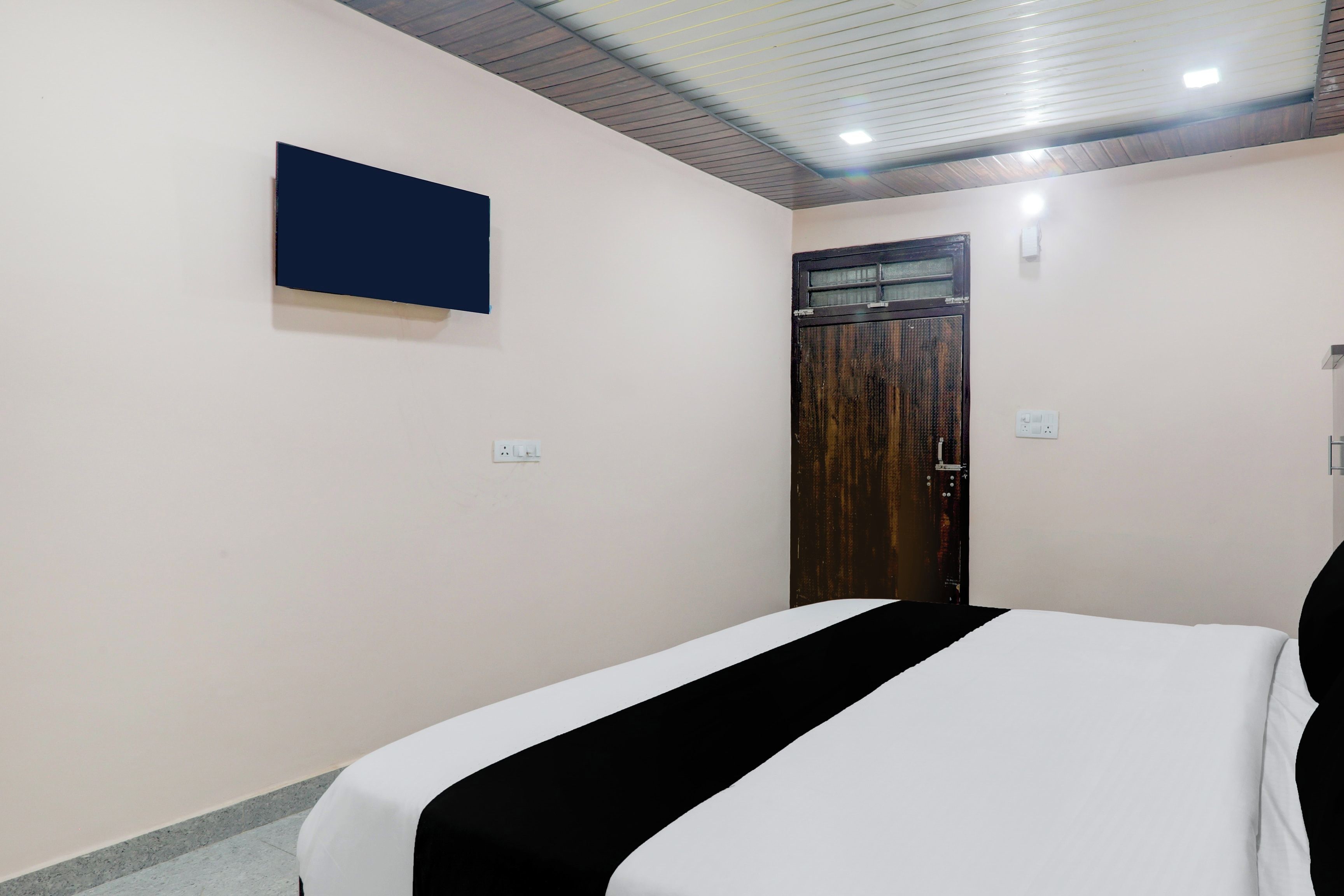 Ein Hotelzimmer mit einem Bett, einem an der Wand befestigten Fernseher und einer Tür mit einem Fenster.