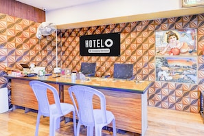 A hotel reception desk with a 'HOTEL O' sign, two white plastic chairs, a computer, and a fan. - Hotel O Poigai Near Airport (Chennai)