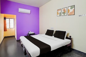 A hotel room with a bed, a nightstand, an air conditioning unit, a window with curtains, and wall-mounted artwork. - Hotel O Poigai Near Airport (Chennai)
