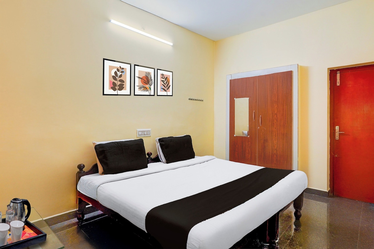 A hotel room with a bed, a wooden wardrobe, a red door, and three framed pictures on the wall.