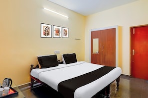 A hotel room with a bed, a wooden wardrobe, a red door, and three framed pictures on the wall. - Hotel O Poigai Near Airport (Chennai)