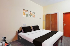 A bedroom with a bed, a wardrobe, and a wall-mounted power outlet. - Hotel O Poigai Near Airport (Chennai)