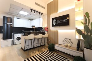 Eine moderne Küche mit integriertem Waschtrockner, einer Bar mit Hockern und einem montierten Fernseher, der 'ELITE LUX HOLIDAY HOMES' zeigt.