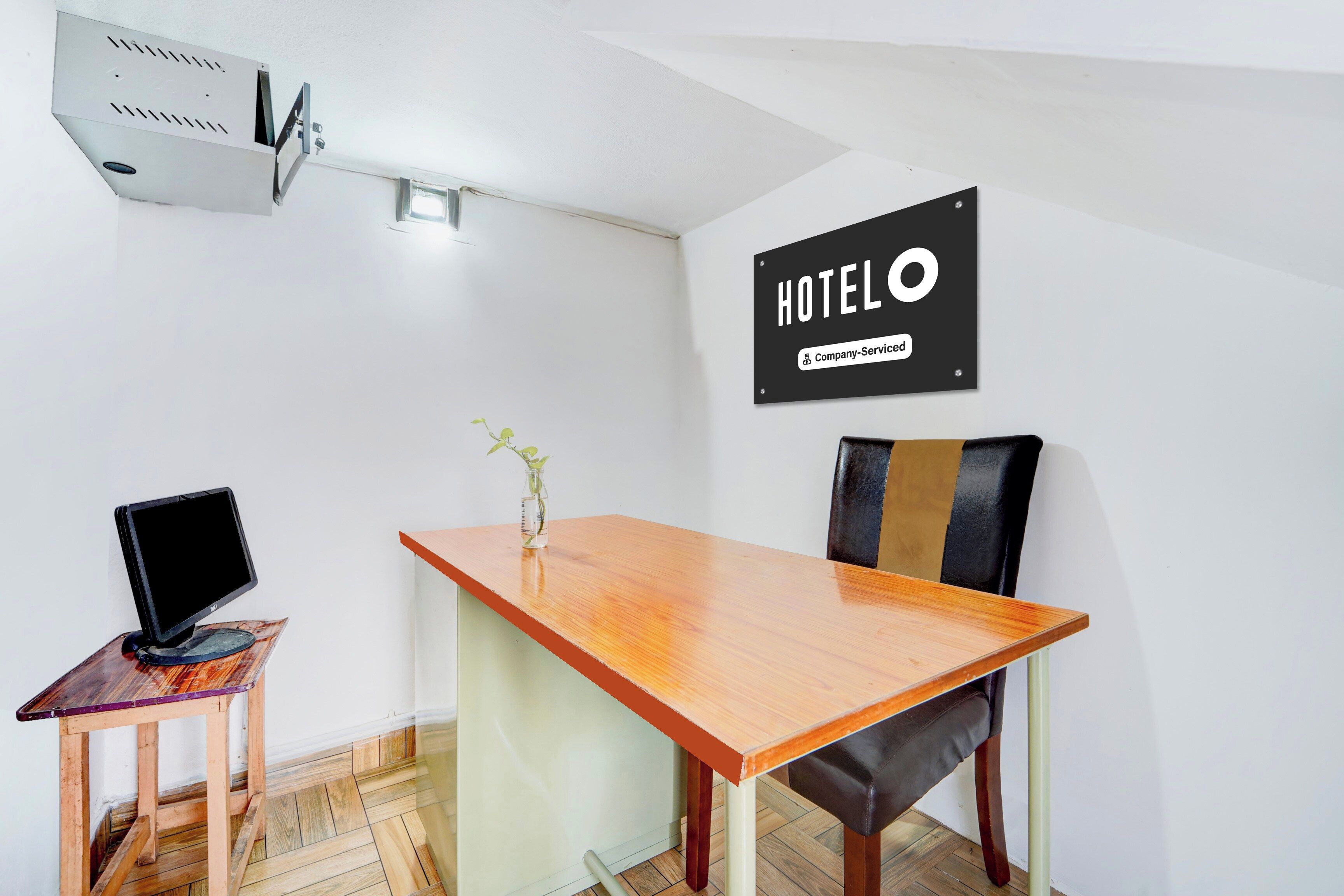 Habitación de hotel con una mesa de madera, una computadora portátil, una silla, una planta pequeña y un cartel que indica que el cuarto cuenta con servicio de la empresa.