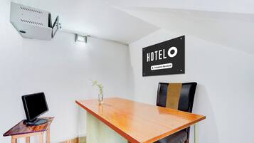 Habitación de hotel con una mesa de madera, una computadora portátil, una silla, una planta pequeña y un cartel que indica que el cuarto cuenta con servicio de la empresa.