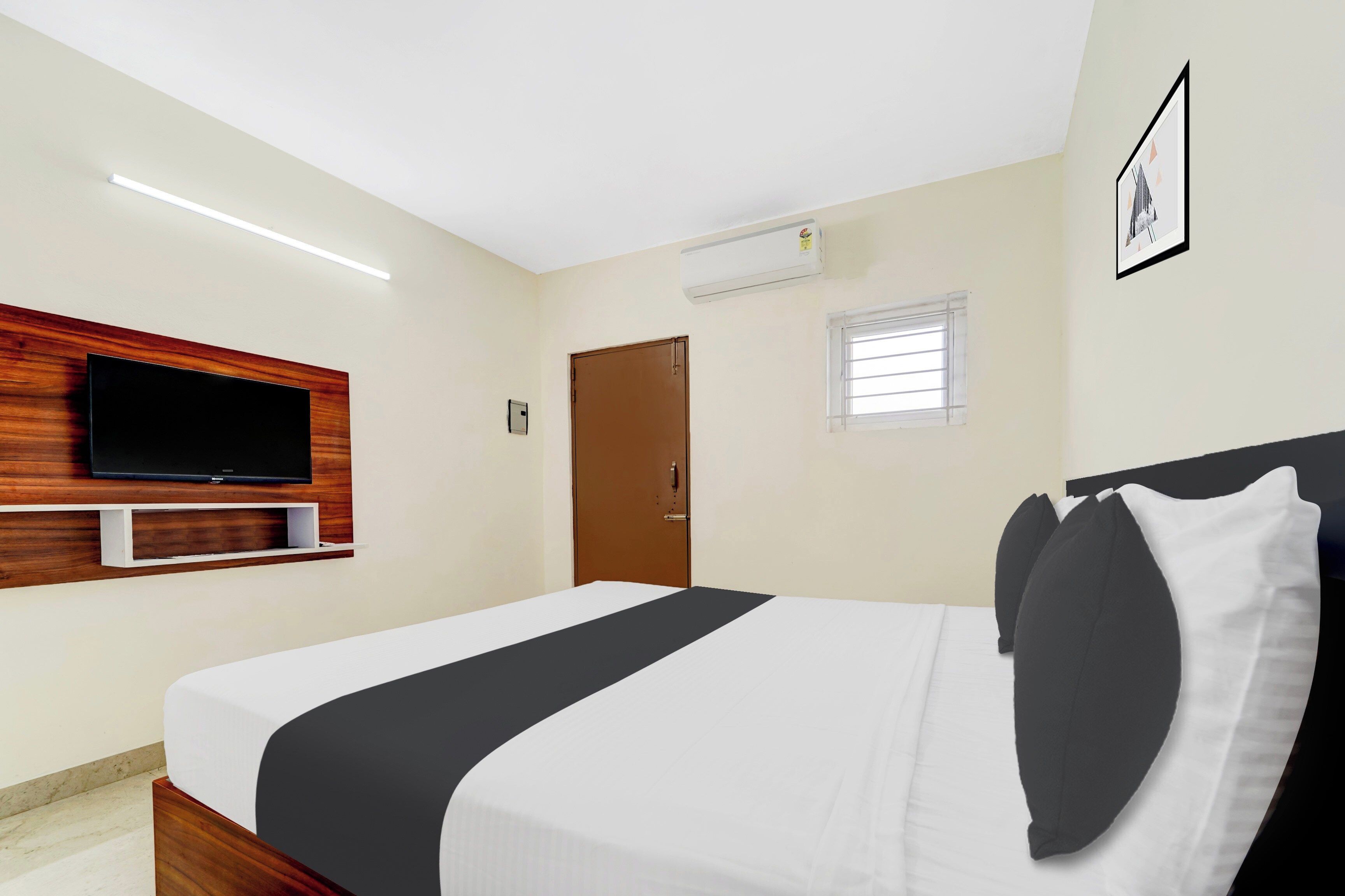 Habitación de hotel con cama, televisor montado en un panel de madera, ventana con persianas y unidad de aire acondicionado en la pared.