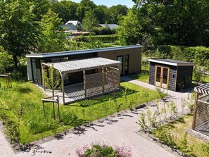 A modern outdoor structure with a covered seating area and a small adjacent building, surrounded by lush greenery. - Luxury Holiday Home Surrounded by Water and Forest (Sint Nicolaasga)