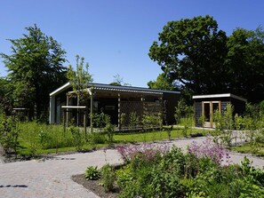 Ein modernes Gebäude mit einer überdachten Terrasse, umgeben von üppigem Grün und einem gepflasterten Weg.