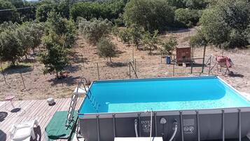 Ein Außenpool mit Holzterrasse, Liegestühlen und Blick auf eine hügelige Landschaft mit Bäumen.