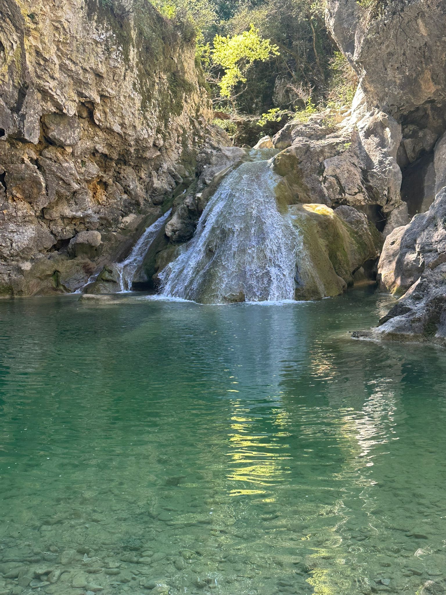 Een waterval stort in een helder poel, omringd door rotsachtig terrein.