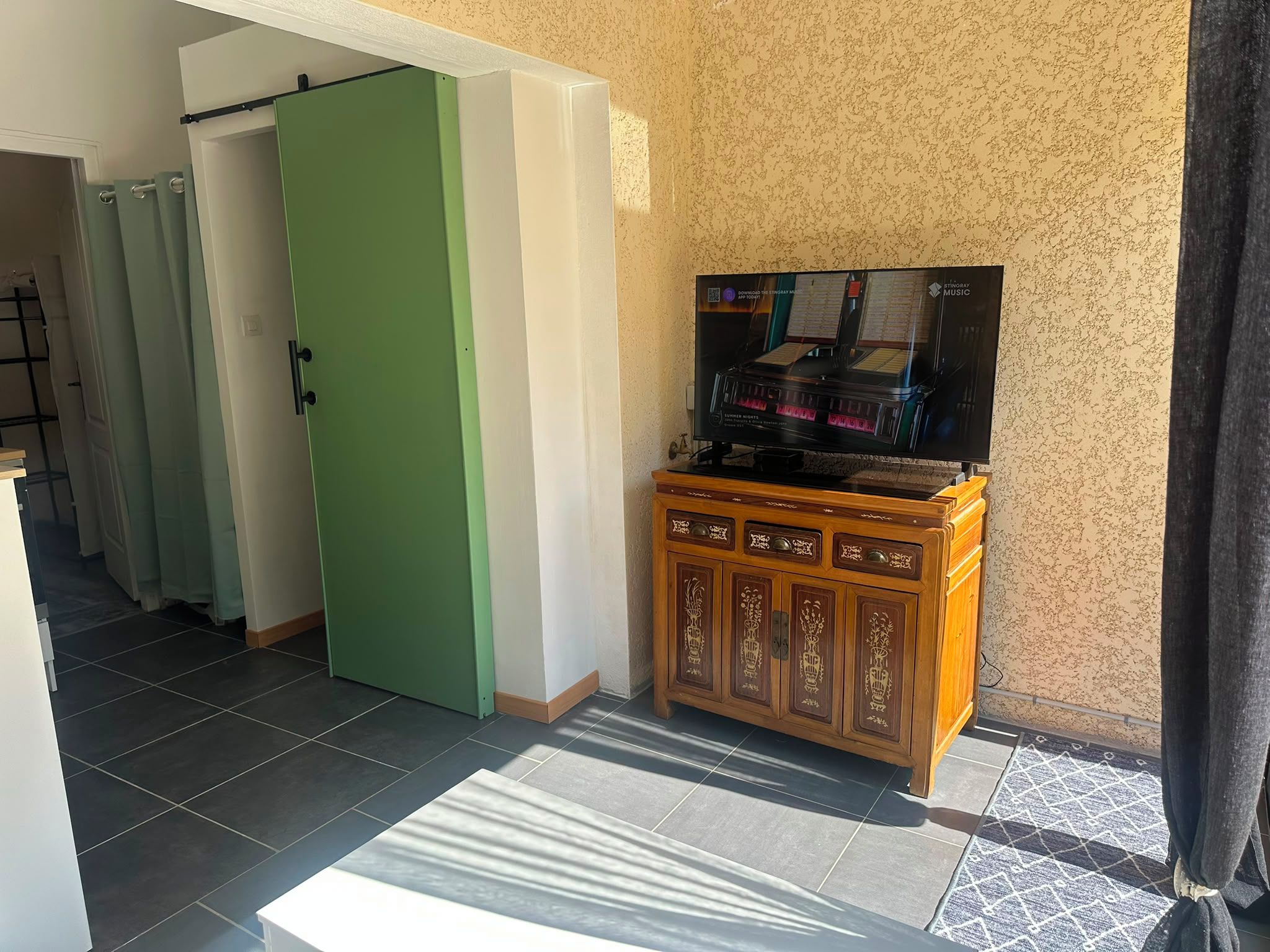 Een kamer met een groene deur, een houten kast met decoratieve panelen en een flatscreen televisie erboven.