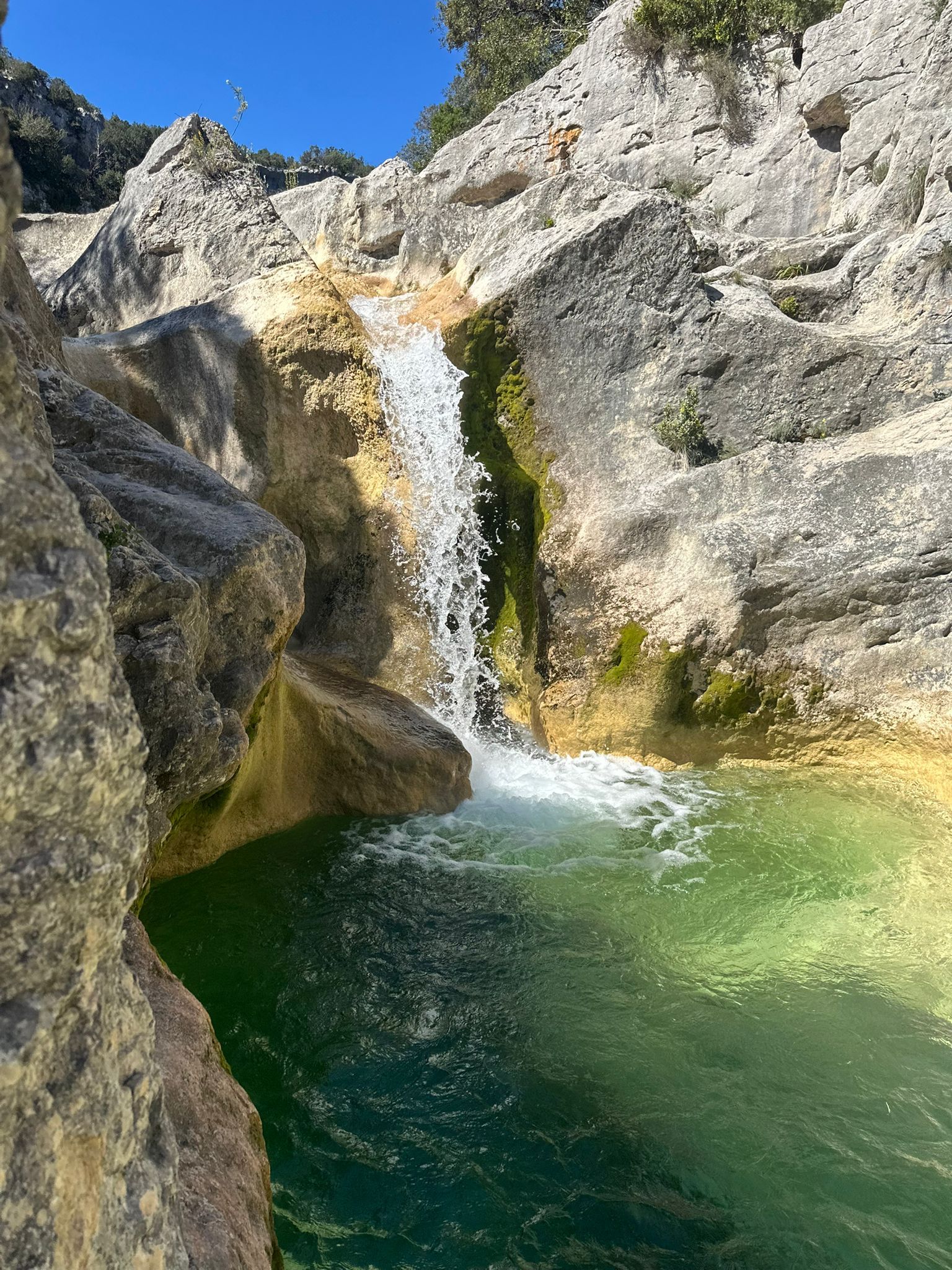 A natural waterfall cascading into a clear pool surrounded by rocky terrain.
