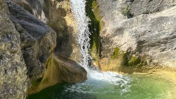 A natural waterfall cascading into a clear pool surrounded by rocky terrain.