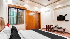Ein Hotelzimmer mit einem Bett, einer Holztür, einem Fernseher, einem kleinen Tisch mit Wasserkocher und einem Sessel.