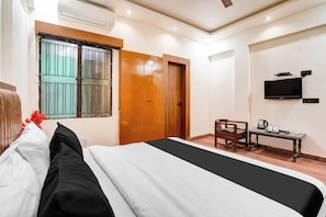 Camera d'albergo con un letto, una porta in legno, una televisione, un tavolino con un bollitore e una sedia.