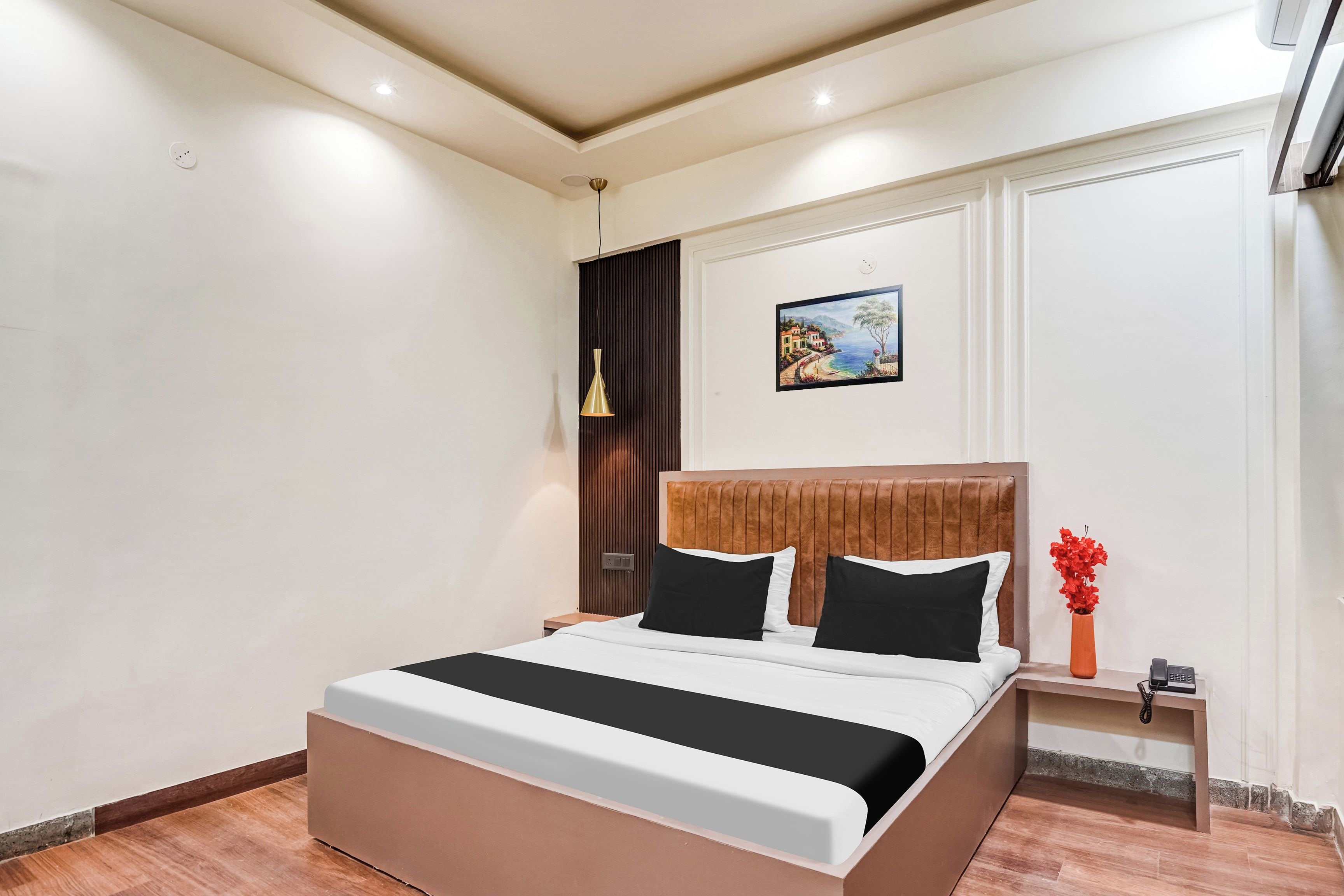 Ein modernes Hotelzimmer mit einem großen Bett, einem Gemälde an der Wand und einem Nachttisch mit einem Telefon.