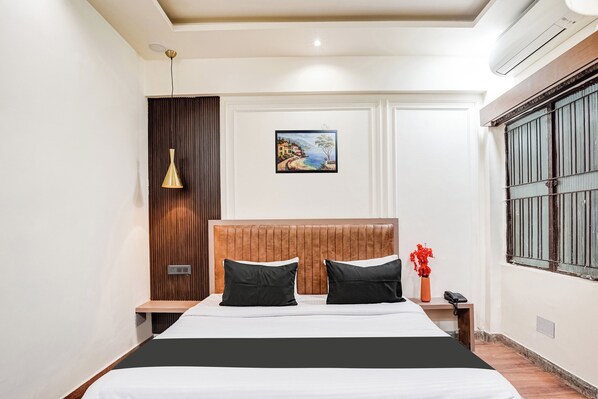 A bedroom with a bed, bedside tables, a wall-mounted painting, a window with bars, and a hanging light fixture. - OYO Collection O Ratan Lal Nagar (Kanpur)