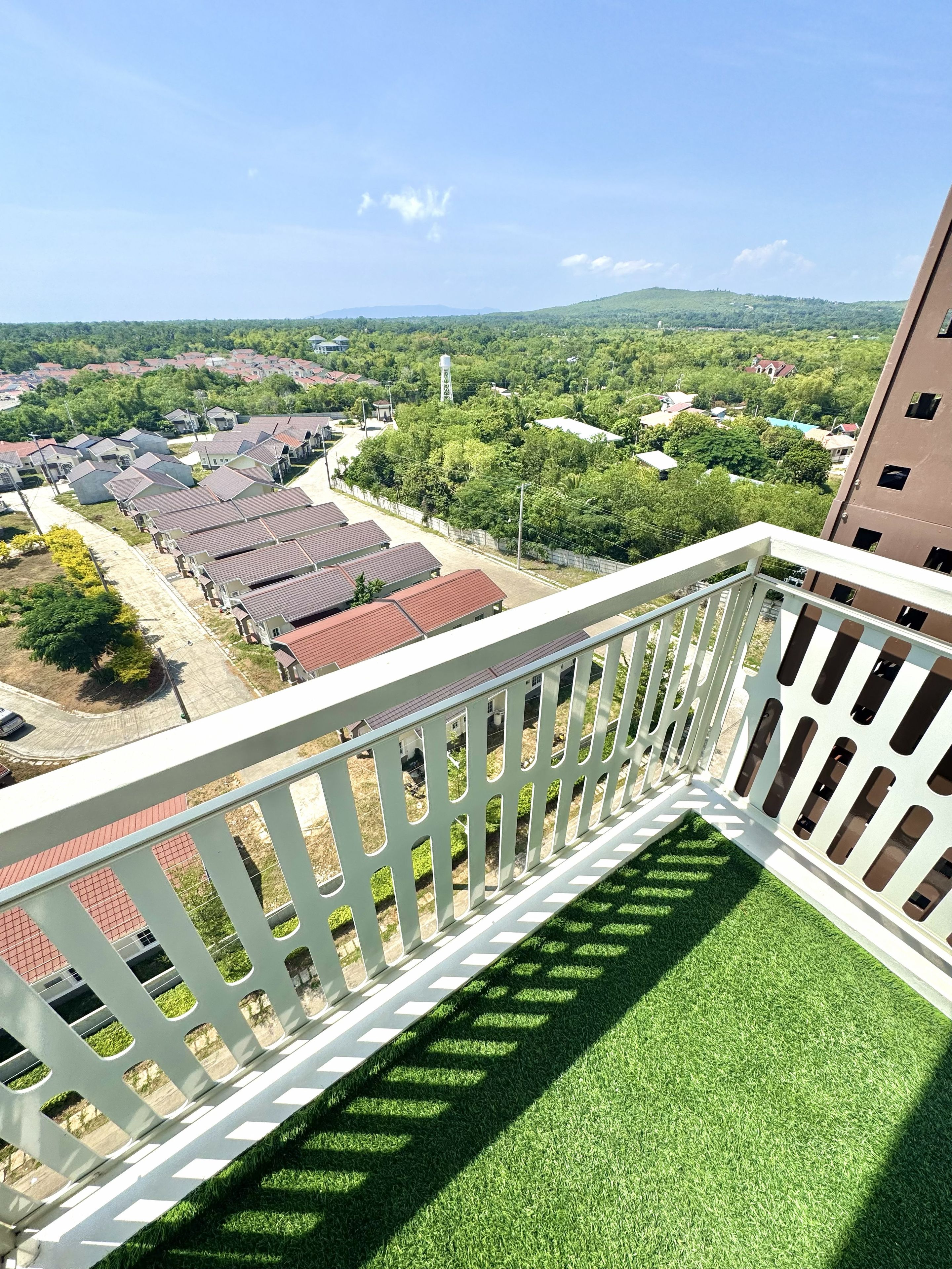 Un balcon doté d’une balustrade blanche, donnant sur un quartier résidentiel avec des maisons et de la verdure.