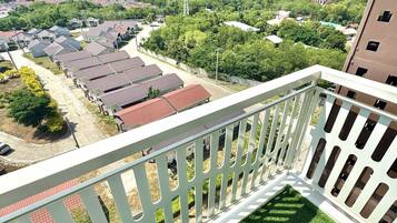 A balcony with a white railing overlooking a residential area with houses and greenery.