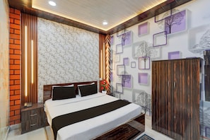 A hotel room with a bed, a wardrobe, a nightstand, and a wall with a floral pattern.