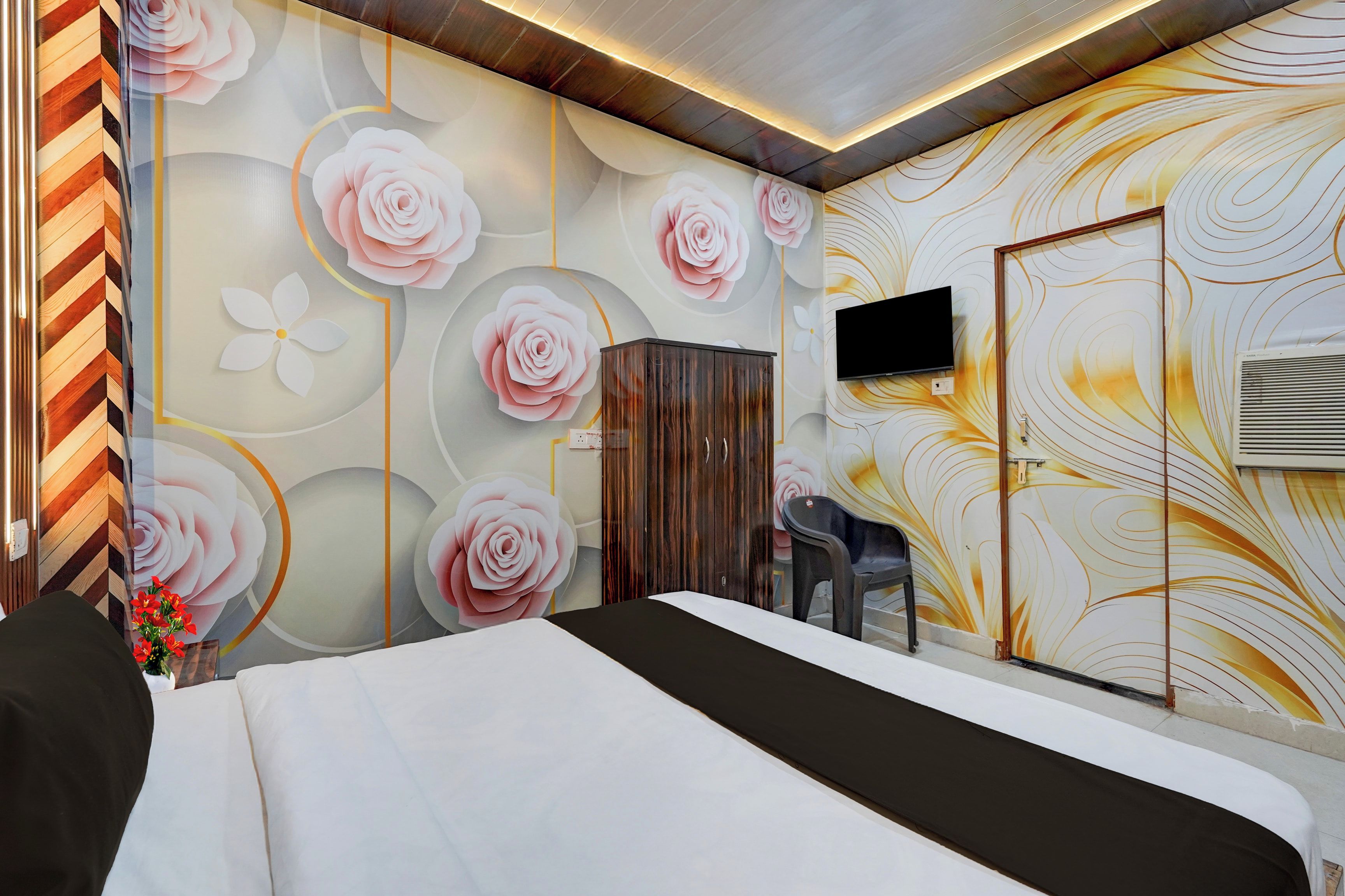 A hotel room with a bed, a TV mounted on the wall, and a decorative wall with floral patterns.