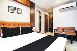 A hotel room with a large bed, a sofa, a desk, and a wall-mounted air conditioner. - Super Hotel O Tagore Park Laskarhat (Kolkata)