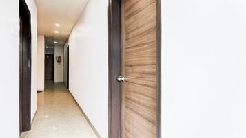 A hallway with a wooden door on the right, a fire extinguisher on the wall, and a door at the end.